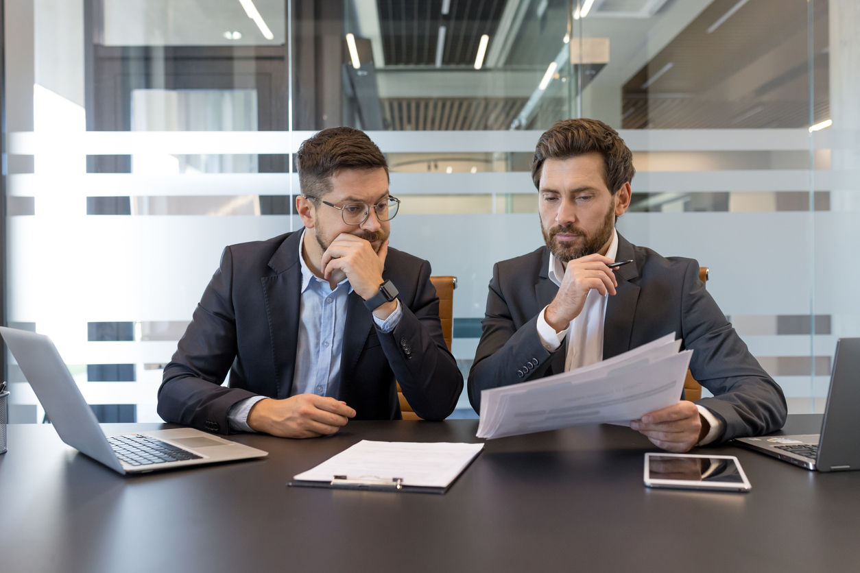 Two professional businessmen discussing documents and engaging in a focused collaboration, reviewing financial reports and making important decisions during an office meeting